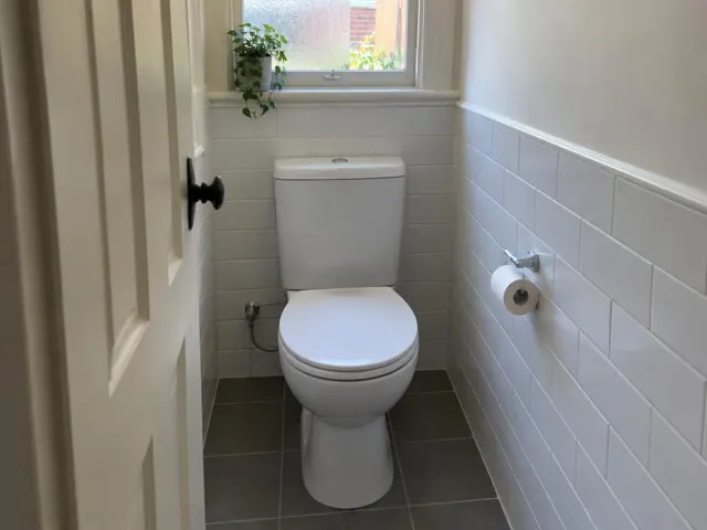 Clean white toilet in a tiled small bathroom with window light in Leichhardt
